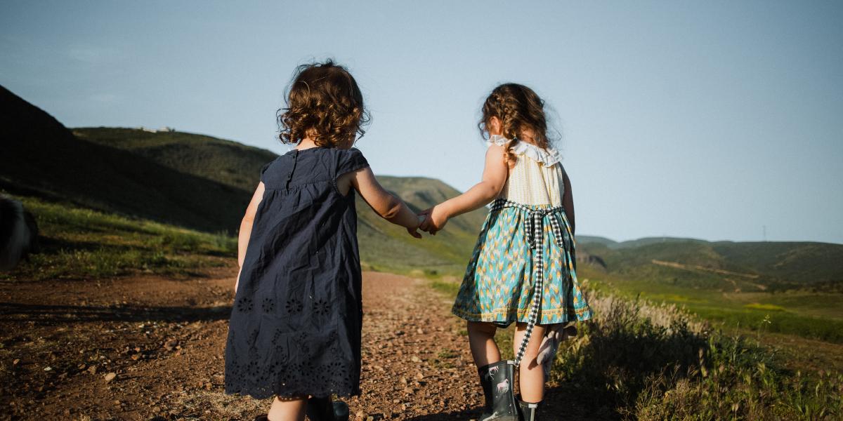 An image of 2 female children holding hands going for a walk